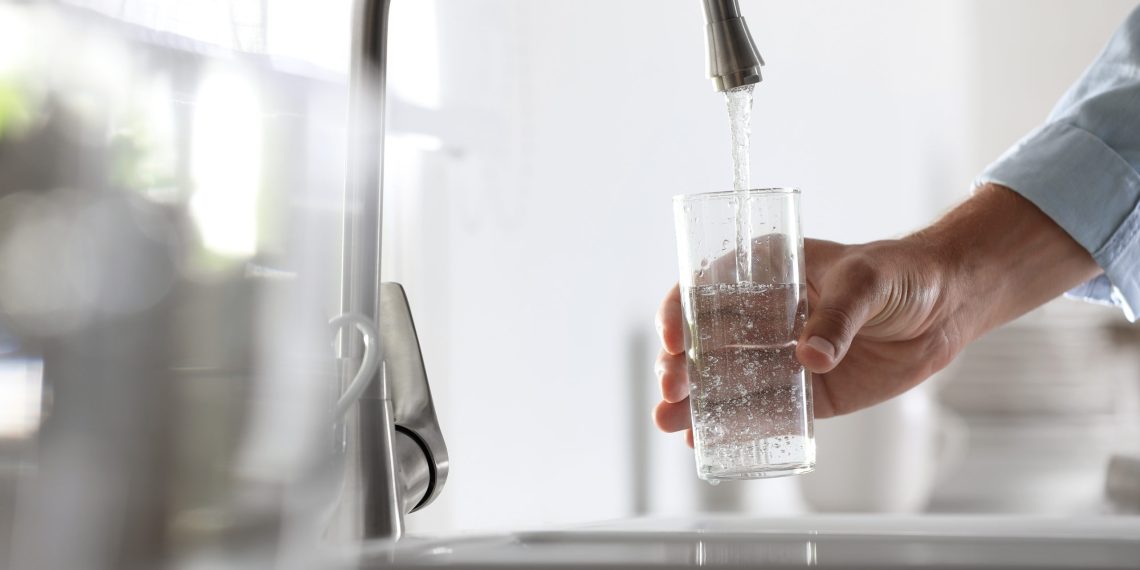 Man pouring water into glass in kitchen, closeup