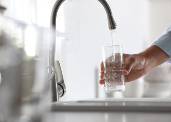 Man pouring water into glass in kitchen, closeup
