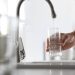 Man pouring water into glass in kitchen, closeup