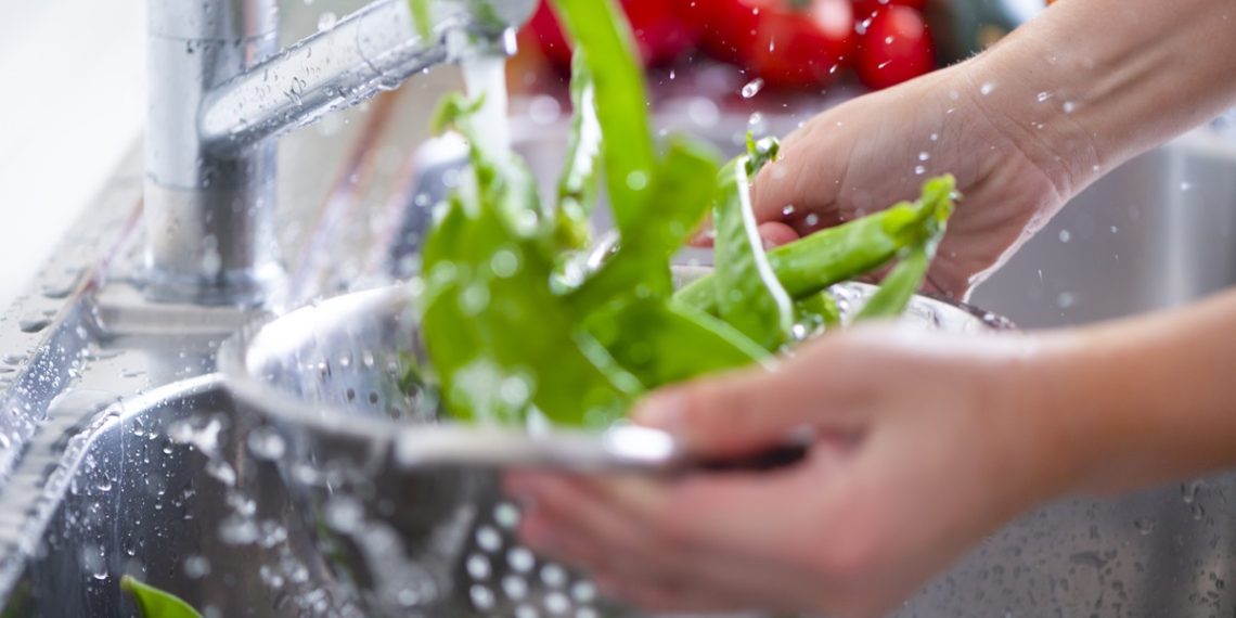 Woman Washing bright green snow peas in a colander in the sink.