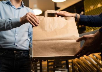 Man in shirt picking a takeaway food package from a restaurant. Blank craft paper box with room for text or logo. Crop shot, unrecognizable faces.