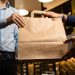 Man in shirt picking a takeaway food package from a restaurant. Blank craft paper box with room for text or logo. Crop shot, unrecognizable faces.