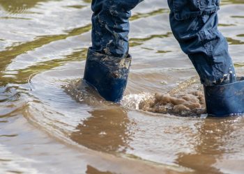 Young boy with short blue trowsers wading with wet socks and wet boots through high tide after a floodwater has broken the dike and overflown the lands behind