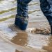 Young boy with short blue trowsers wading with wet socks and wet boots through high tide after a floodwater has broken the dike and overflown the lands behind
