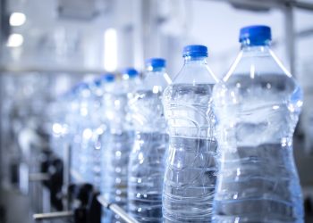 Close up view on plastic bottles of water in bottling factory being transported by conveyor belt automated machine.