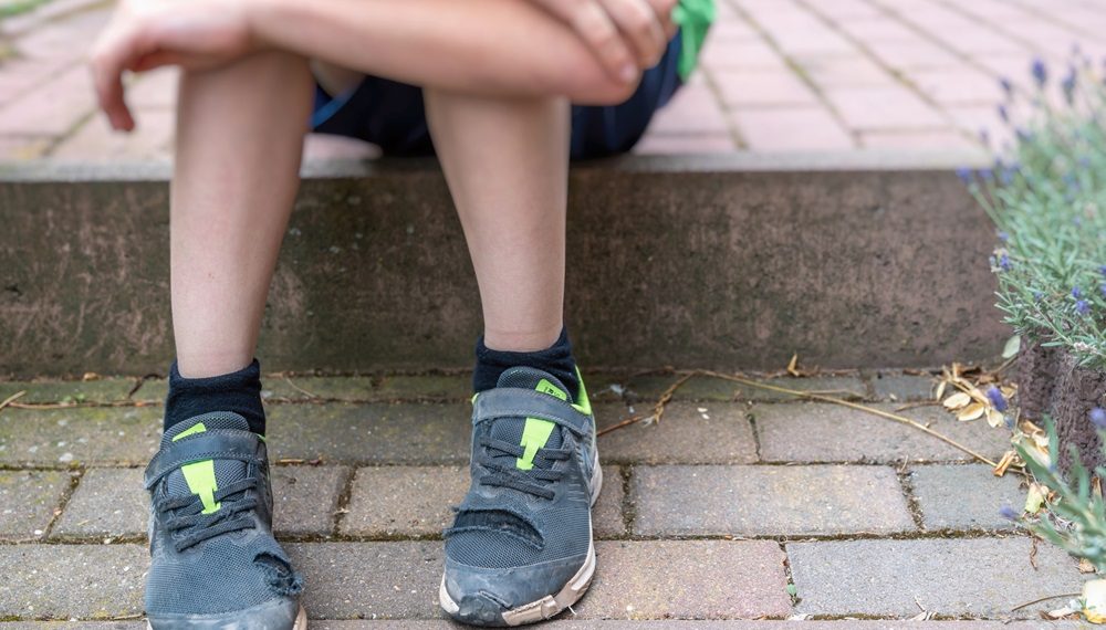 Little boy with broken shoes as a symbol of child poverty