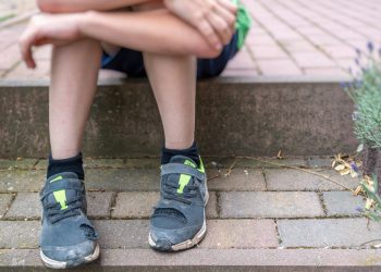 Little boy with broken shoes as a symbol of child poverty