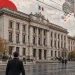 Palazzo ministeriale a Roma sotto un cielo grigio, cavi elettrici e persone di spalle sul marciapiede